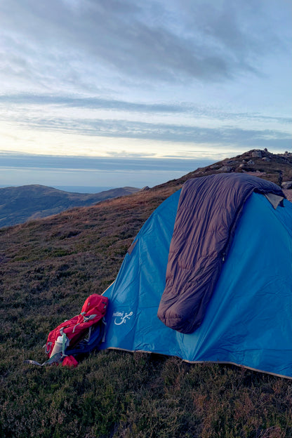 Tente 3 personnes Isis 3, marque Freetime, vue en fin de journée, sur un plateau de montagne, avec sac de couchage Lodenn posé dessus.
Crédit @cestmeline