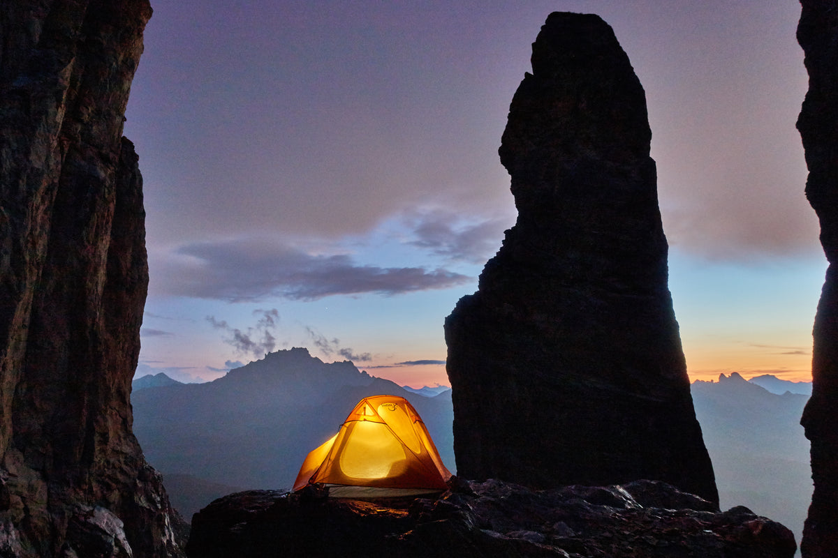 Mountain 2DLX – Tente légère pour 2 personnes - marque Freetime – vue au crépuscule avec une lumière allumée dans la tente qui est au pied d'un pic rocheux
Crédit : @sebas_langlais