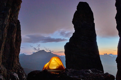 Mountain 2DLX – Tente légère pour 2 personnes - marque Freetime – vue au crépuscule avec une lumière allumée dans la tente qui est au pied d'un pic rocheux
Crédit : @sebas_langlais