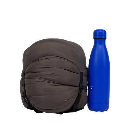 Sac de couchage Lodenn, marque Freetime, duvet température confort -1°C pour moins de 1kg ! vue compressé au maximum à côté d'une gourde de 500 ml (photo détourée)