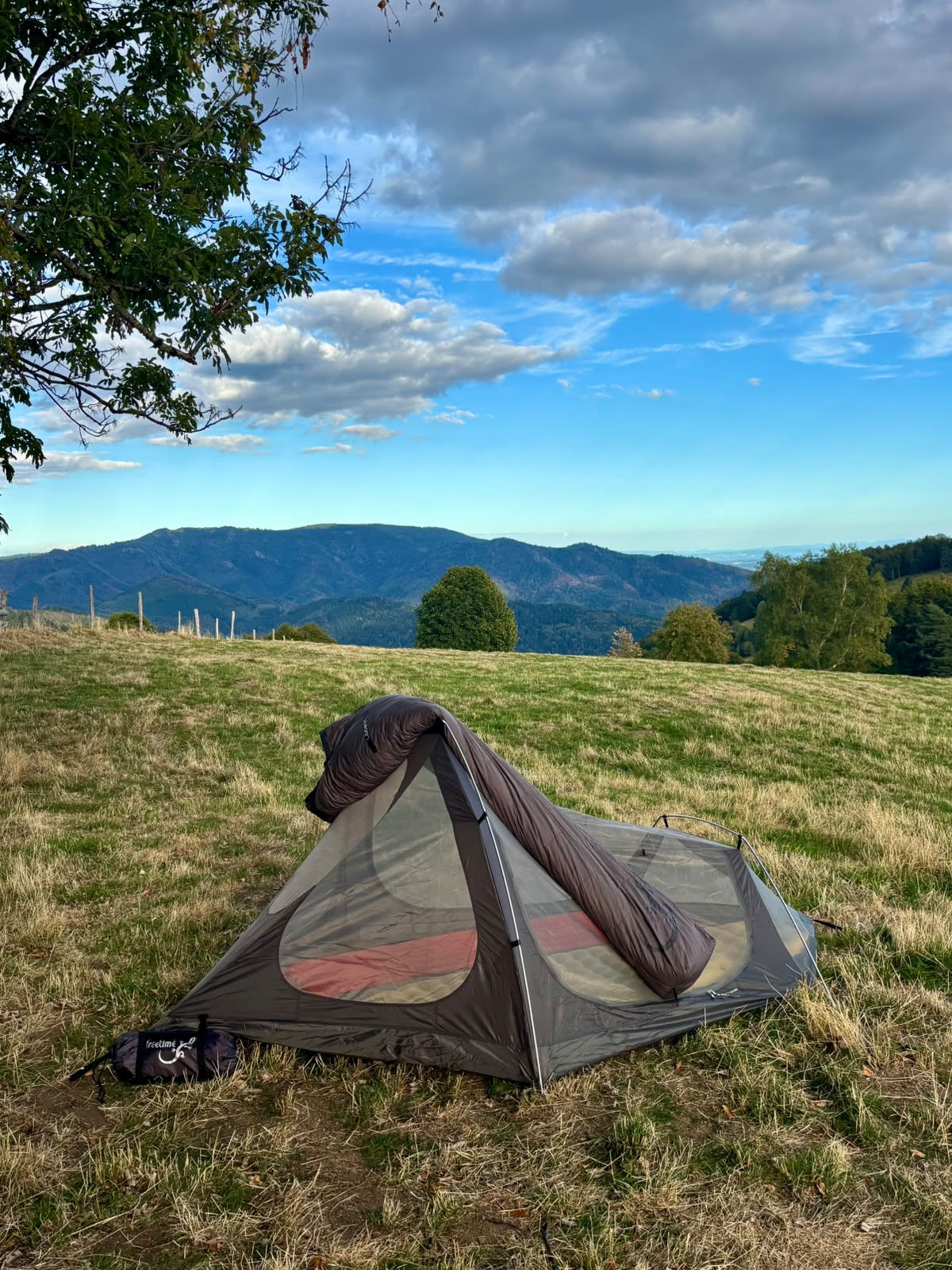 Sac de couchage Lodenn, marque Freetime, duvet température confort -1°C pour moins de 1kg ! vue sur posé sur une tente, dans une clairière, avec un paysage montagneux au loin