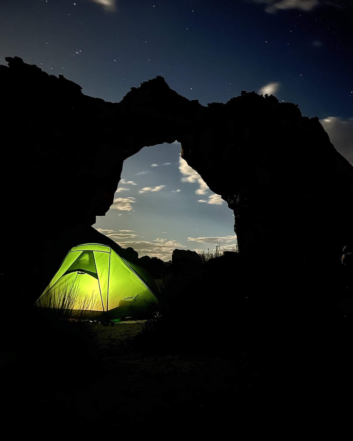 Tente de trek 2 personnes Raidlite 2 DLX de la marque Freetime, de couleur vert forêt, montée au pied d'une arche naturelle en Afrique du Sud, photo de nuit avec lumière allumée dans la tente.
Crédit @bestregardsfromfar